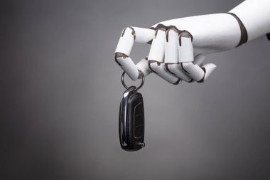 Arabanın anahtarını gri arka plan üzerinde tutan bir Robot Close-Up