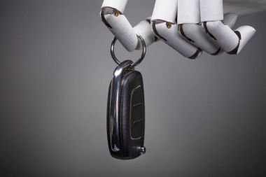 Arabanın anahtarını gri arka plan üzerinde tutan bir Robot Close-Up