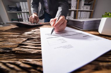 Ahşap masa üzerinde belge imzalarken hesap makinesini kullanarak bir işadamının'ın el Close-Up