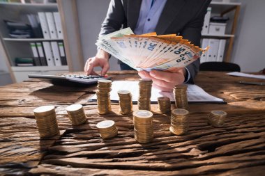 İşadamı Euro banknot masa üzerine yığılmış altın sikke ile hesaplama