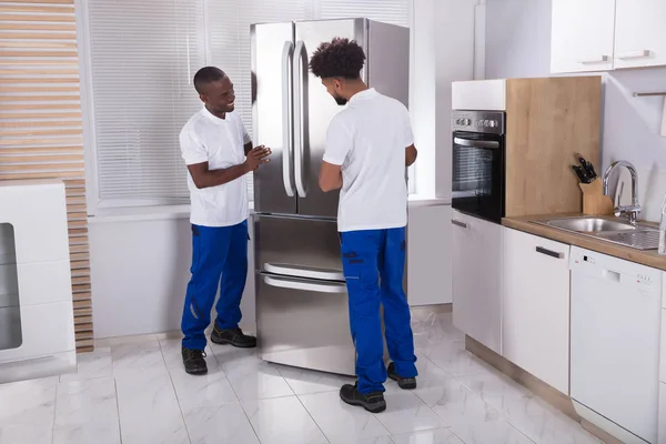 Deux Déménageurs Masculins Uniforme Fixant Congélateur Dans Cuisine Maison — Photo