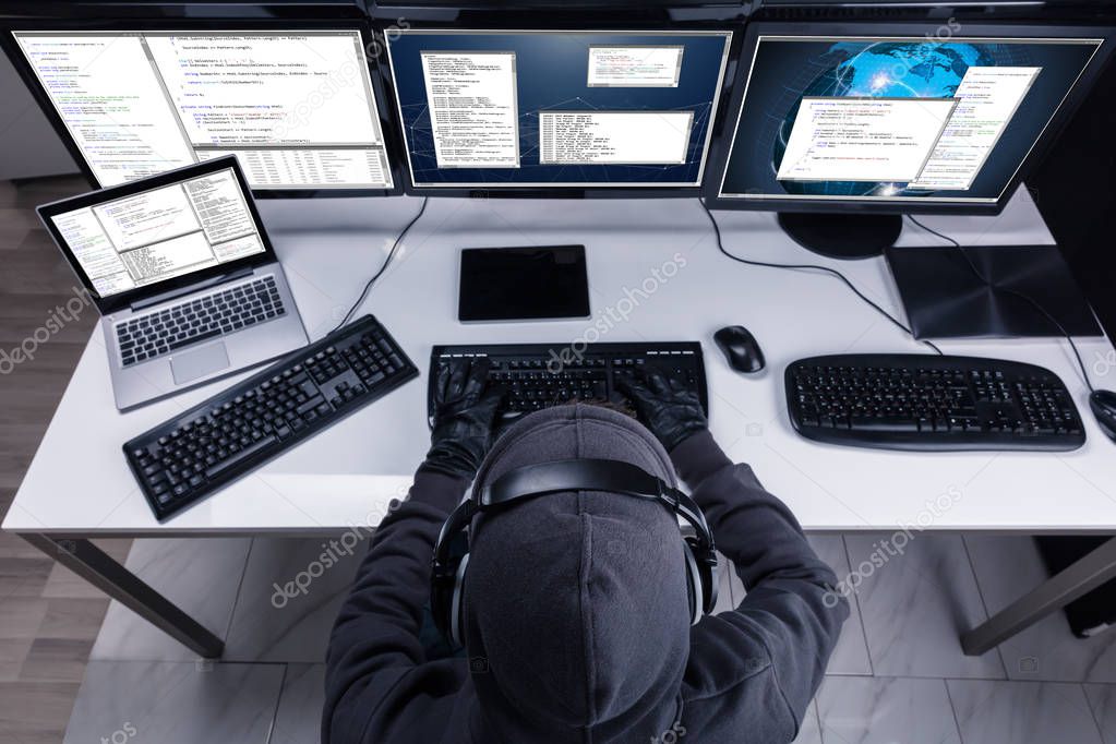 High Angle View Of A Hacker Stealing Information From Multiple Computers In Office