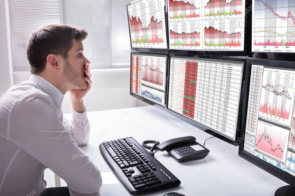 Side View Of A Sad Young Male Operator Looking At Graphs On Multiple Computer Screen