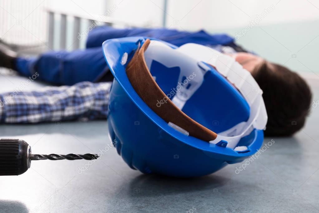 Close-up Of Handyman's Helmet With Unconscious Handyman Lying On Floor