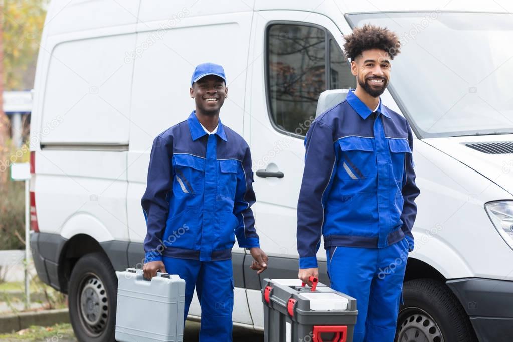 Portrait Of Two Smiling Manual Workers With Their Tool Boxes Standing Near The White Van