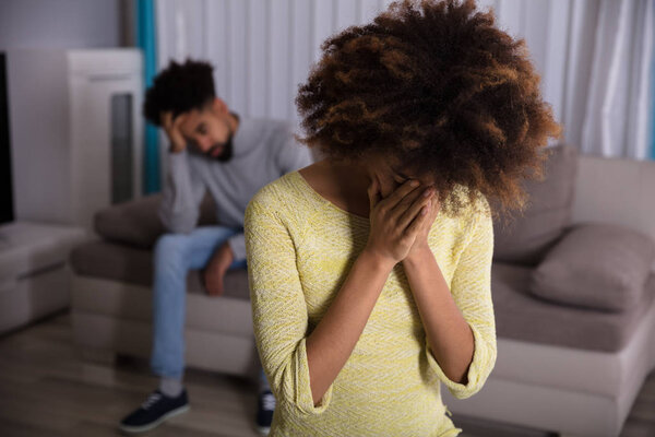 Close-up Of An Unhappy Young Woman In Front Of Man Sitting On Sofa