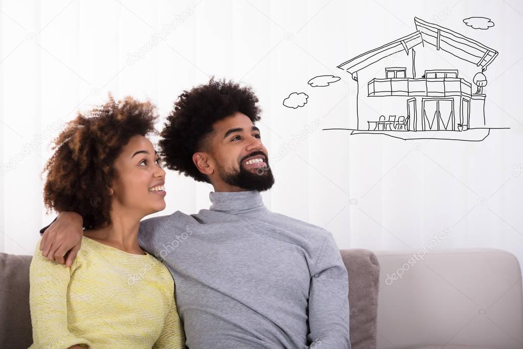 Happy Couple Sitting On Sofa Thinking Of Getting Their Own House