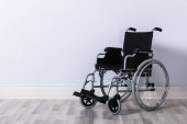 schwarzer, leerer Rollstuhl vor der Wand