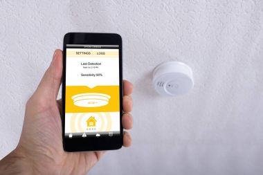 Tavanda cep telefonu duman dedektörü önünde tutan bir insan eli Close-Up