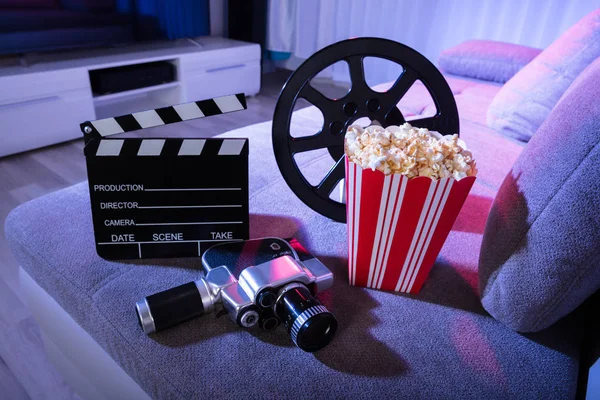 Close-up Of Movie Camera With Clapperboard And Popcorn On Couch At Night