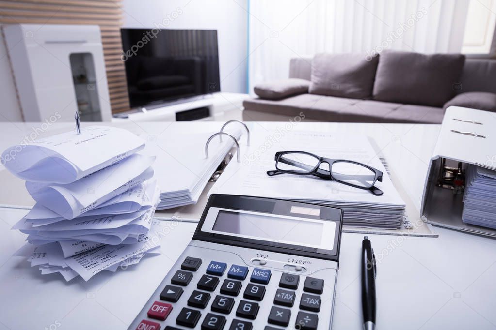 Close-up Of Folders With Receipts And Calculator On White Desk In Bedroom