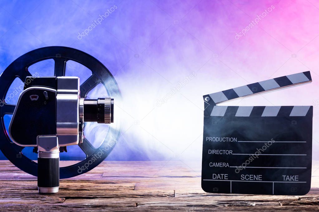 Close-up Of An Illuminated Movie Camera With Film Reel And Clapper Board On Wooden Desk