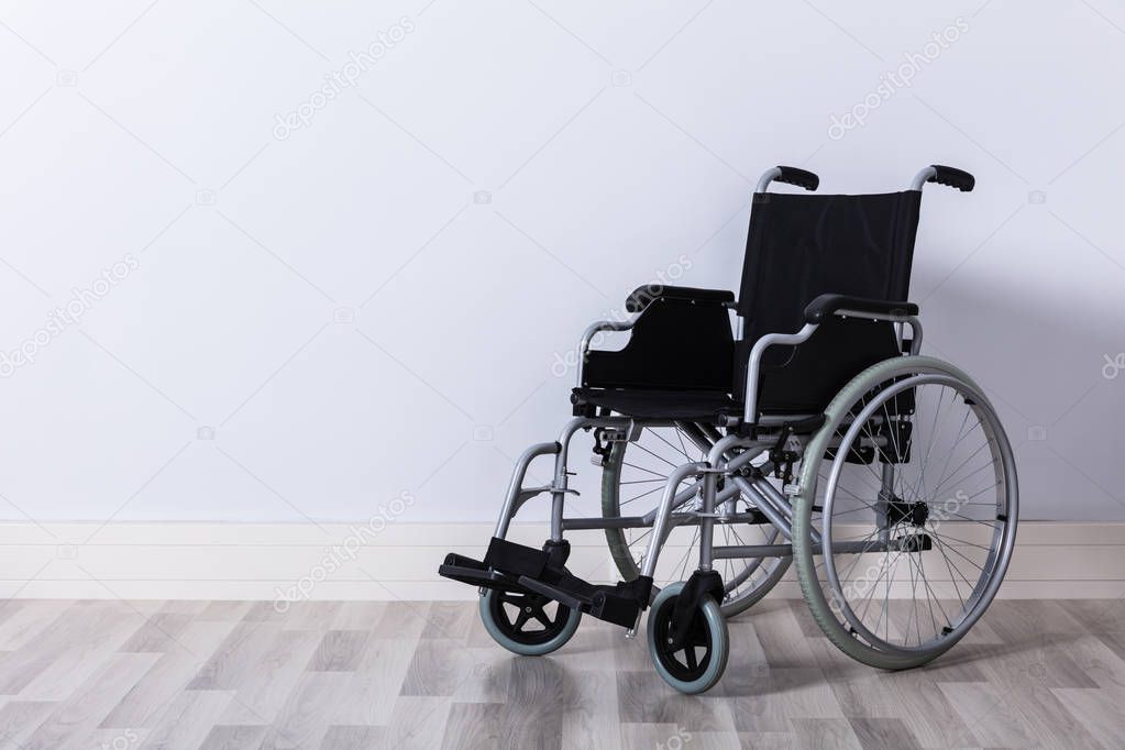 Black Colored Empty Wheelchair In Front Of Wall