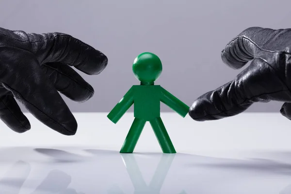 Close Thief Hand Wearing Gloves Stealing Green Human Figure — Stock Photo, Image