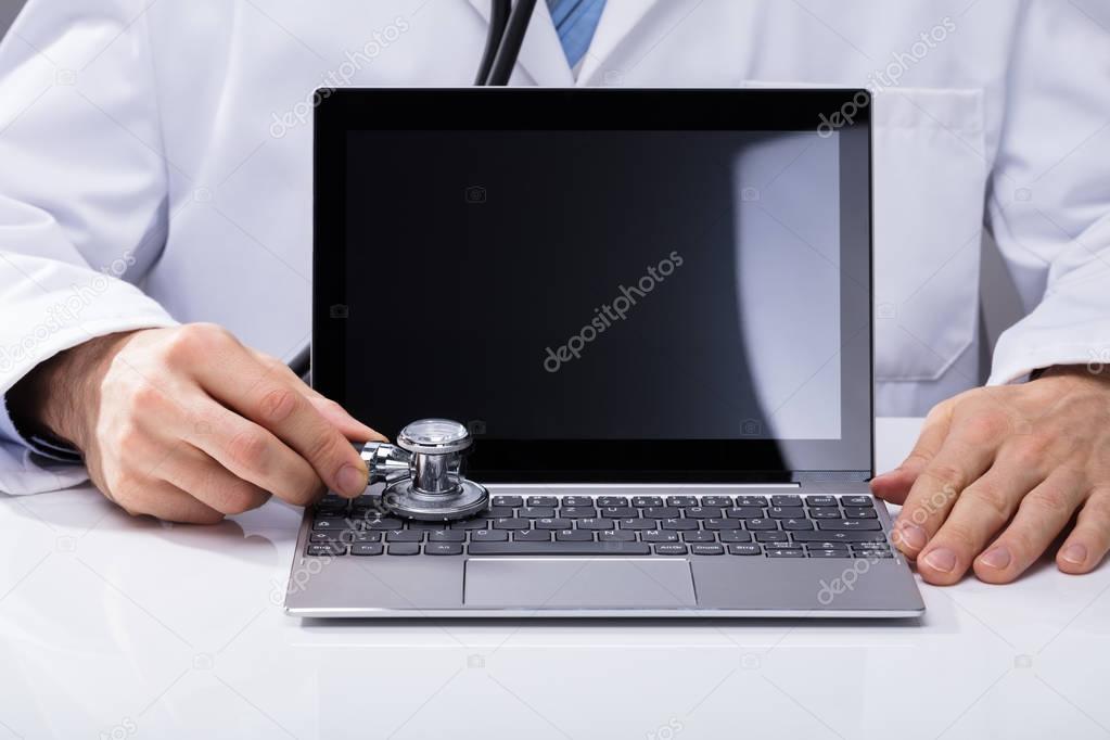 Close-up Of A Doctor's Hand Examining Laptop With Stethoscope