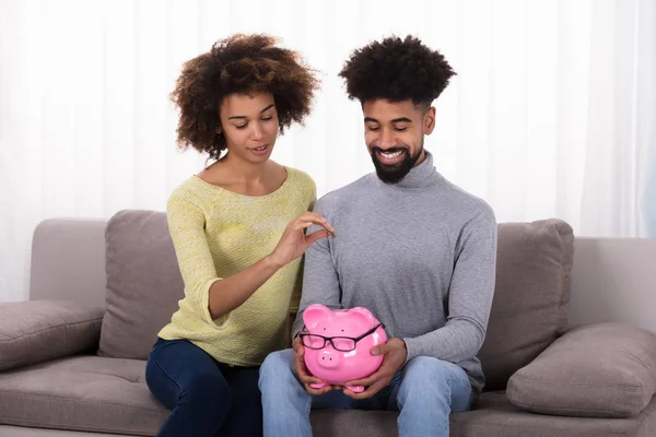 Glückliches Paar Sitzt Auf Sofa Und Steckt Münze Sparschwein — Stockfoto
