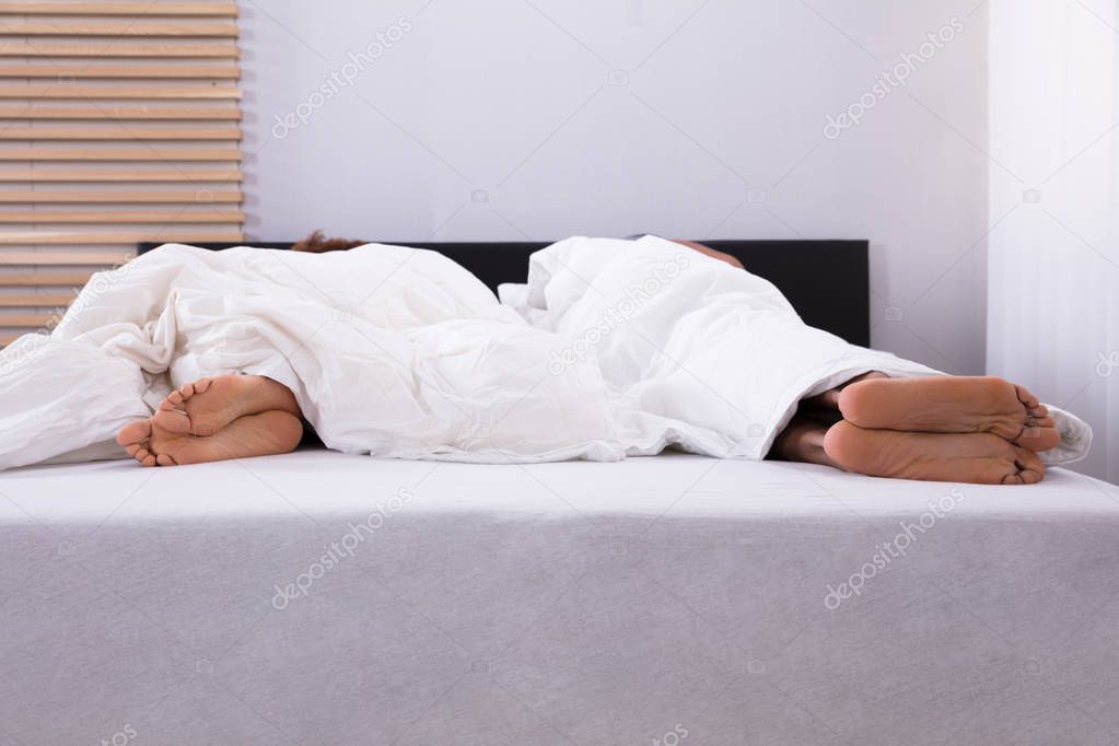 Couple's Feet Sleeping In Bed Under White Sheet