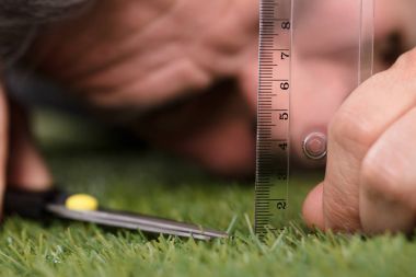 Close-up Of A Man Using Measuring Scale While Cutting Grass With Scissors clipart