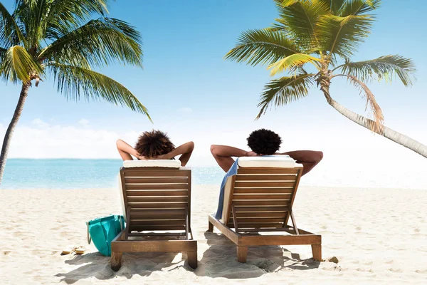 在海滩上的甲板椅上放松的一对年轻夫妇的后视图 — 图库照片