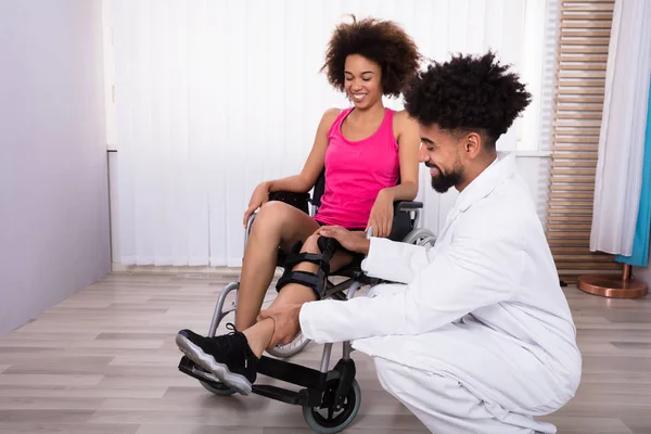 クリニックで女性の脚の膝ブレースを固定若い男性理学療法士 — ストック写真