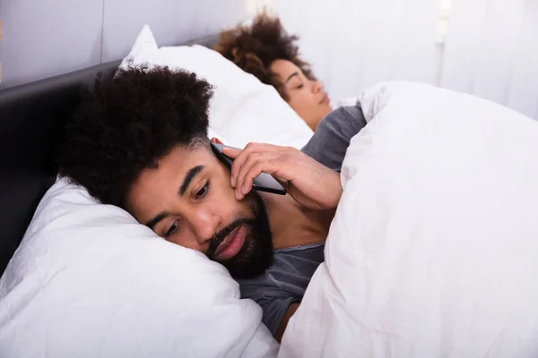 Człowiek Rozmowy Telefon Komórkowy Podczas Gdy Jej Żona Spanie Łóżku — Zdjęcie stockowe