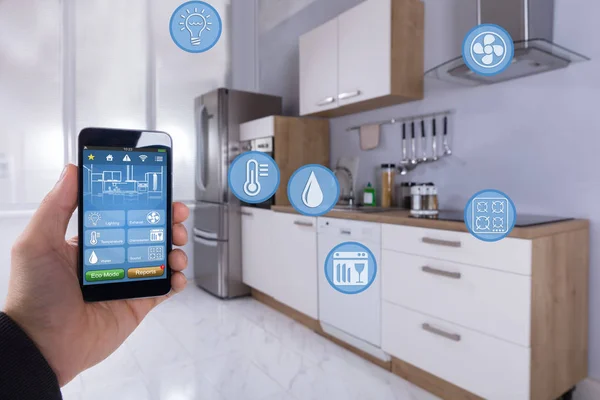 キッチンでスマート フォンでスマート ホーム アプリケーションを使う人の手のクローズ アップ — ストック写真