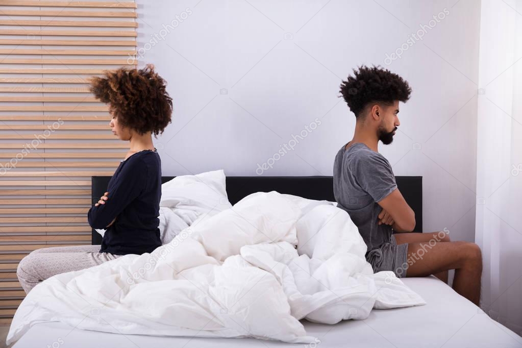 Side View Of Young Couple Sitting On Bed Ignoring Each Other