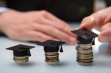 Üzerinde bir satırda yığılmış paralar mezuniyet şapka yerleştirerek bir işadamının'ın el Close-Up