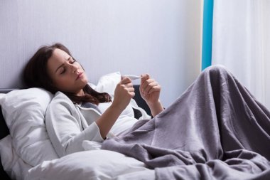 Vücut sıcaklığını termometre ile kontrol yatakta yatan hasta genç kadın