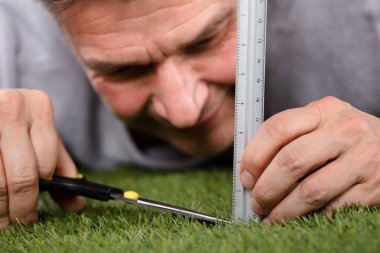 Close-up Of A Man Using Measuring Scale While Cutting Grass With Scissors clipart
