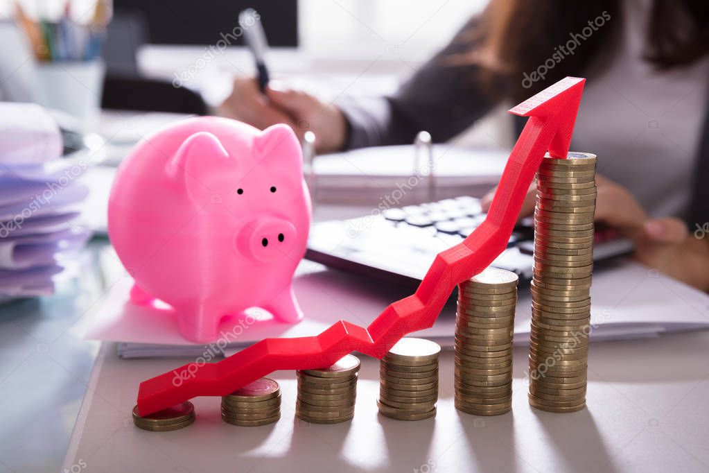 Close-up Of Stacked Coins And Arrow Showing Upward Direction In Front Of Pink Piggybank