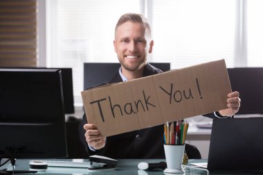 Portrait Of A Smiling Young Businessman Holding Cardboard With Thank You Text clipart