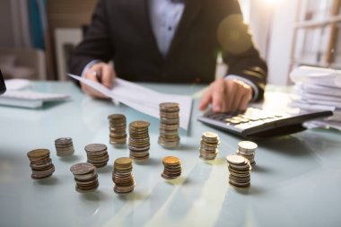 Close-up Of Stacked Coins In Front Of Businessman Working On Document clipart