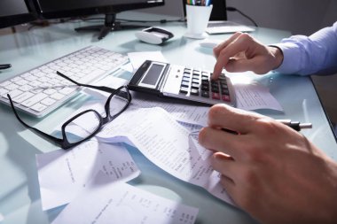 Close-up Of A Businessperson's Hand Calculating Receipt At Workplace clipart