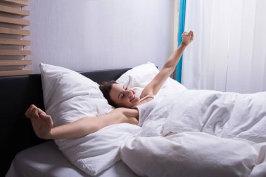 Young Woman Waking Up Stretching Her Hands On Bed clipart