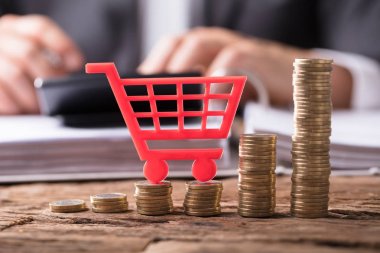 Close-up Of Red Shopping Cart On Stacked Golden Coins Over Wooden Desk clipart