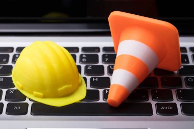 Close-up Of Hard Hat And Traffic Cone On Laptop Keypad clipart