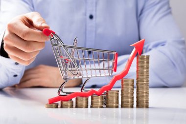 Increasing Graph Of Coins In Front Of Human Hand Holding Small Shopping Cart clipart