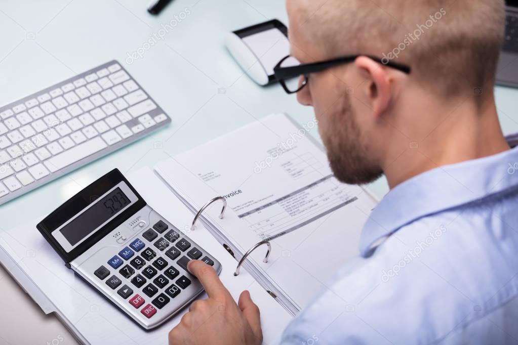 Businessman Using Calculator For Calculating Invoice At Desk