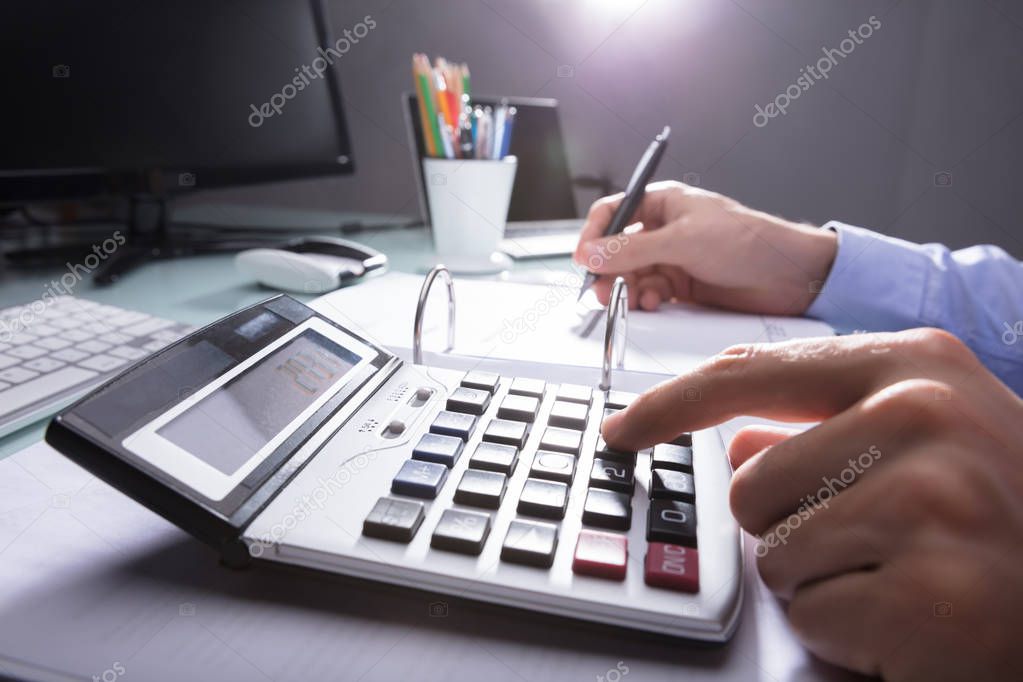 Businessperson's Hand Calculating Receipt With Coins And Eyeglasses On Desk
