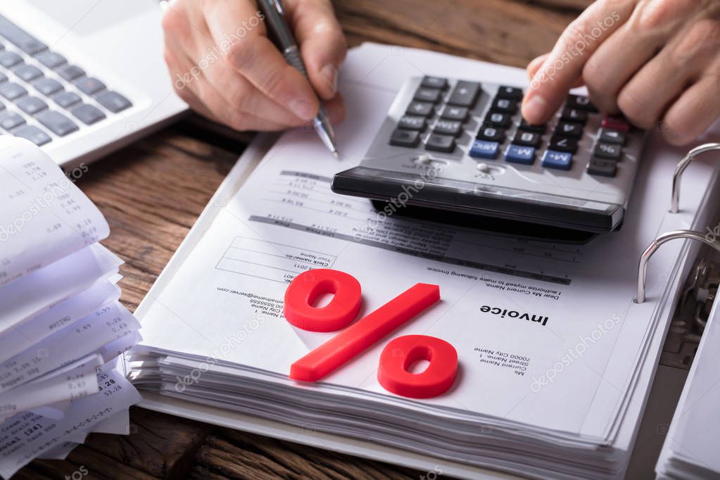 Close-up Of Red Percentage Symbol With Businessperson Calculating Bill