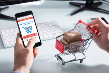 Cep telefonundan alışveriş yaparken karton kutuları olan bir kişinin el arabası.