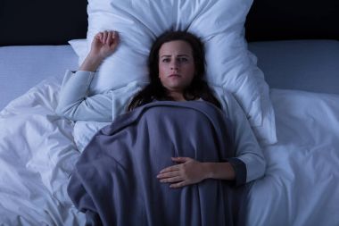 Yükseltilmiş üzücü bir genç kadın yatakta yatarken görünümünü