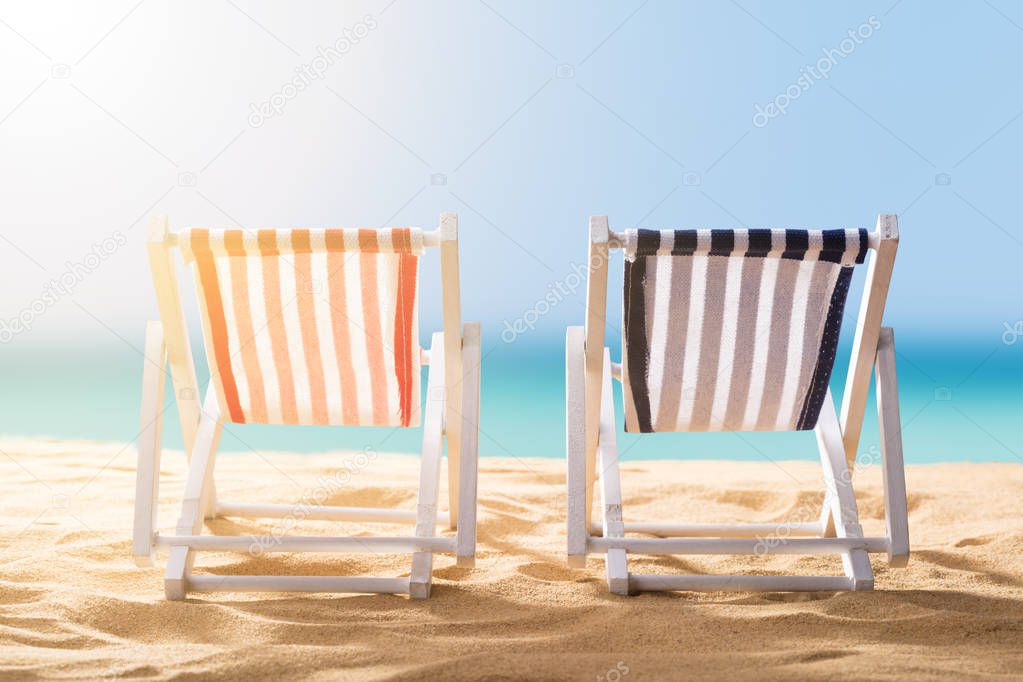 Close-up Of Two Blue And Red Striped Deck Chairs On Sandy Beach