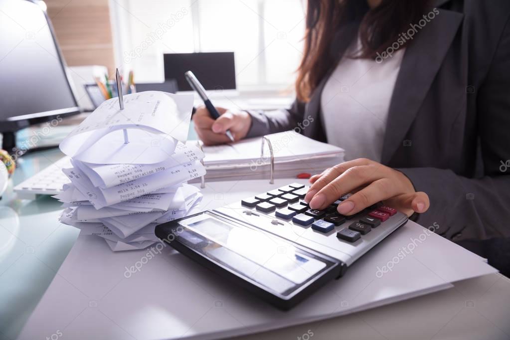 Close-up Of A Businesswoman's Hand Calculating Invoice With Calculator