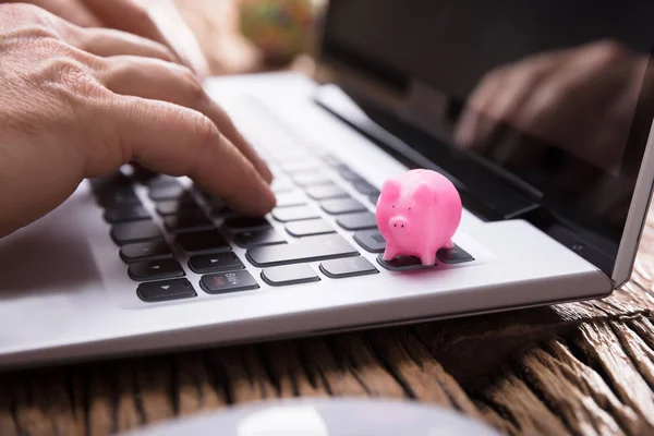 在键盘上使用带有粉红色 Piggybank 的笔记本电脑的一个商人的手特写 — 图库照片
