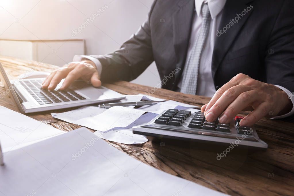 Close-up Of A Businessperson's Hand Using Calculator On Wooden Desk