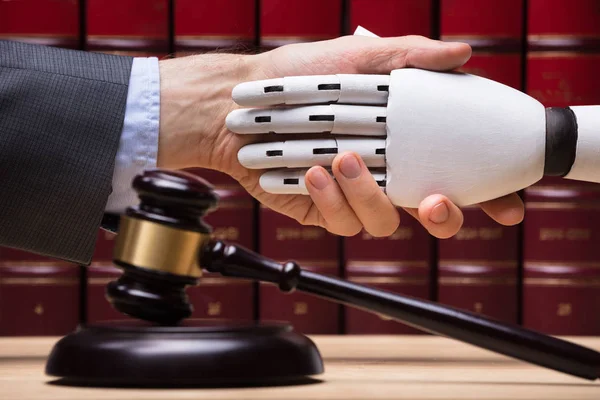 Robot Shaking Hands With Judge Near Gavel On Wooden Desk