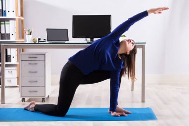 Egzersiz egzersiz mat ofiste yapıyor bir genç iş kadını yan görünüm