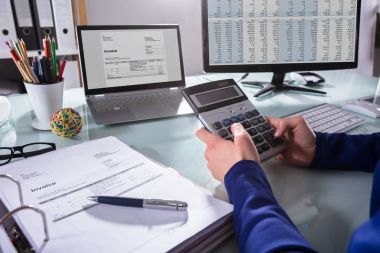 Close-up Of A Businessperson's Hand Calculating Invoice At Workplace clipart